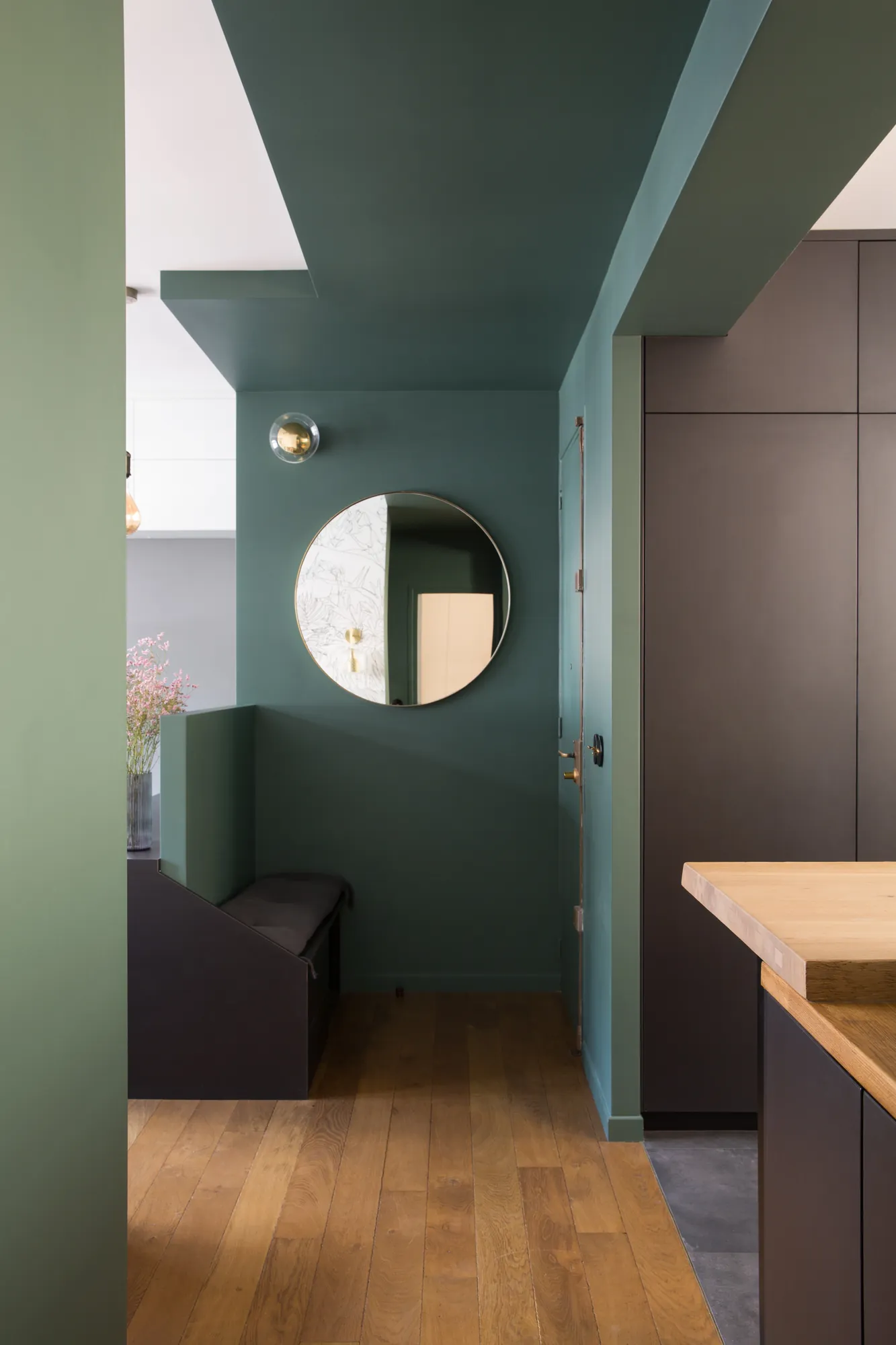 Entrée peinte en vert profond, miroir rond en laiton et coin banc, appartement Paris 15e
